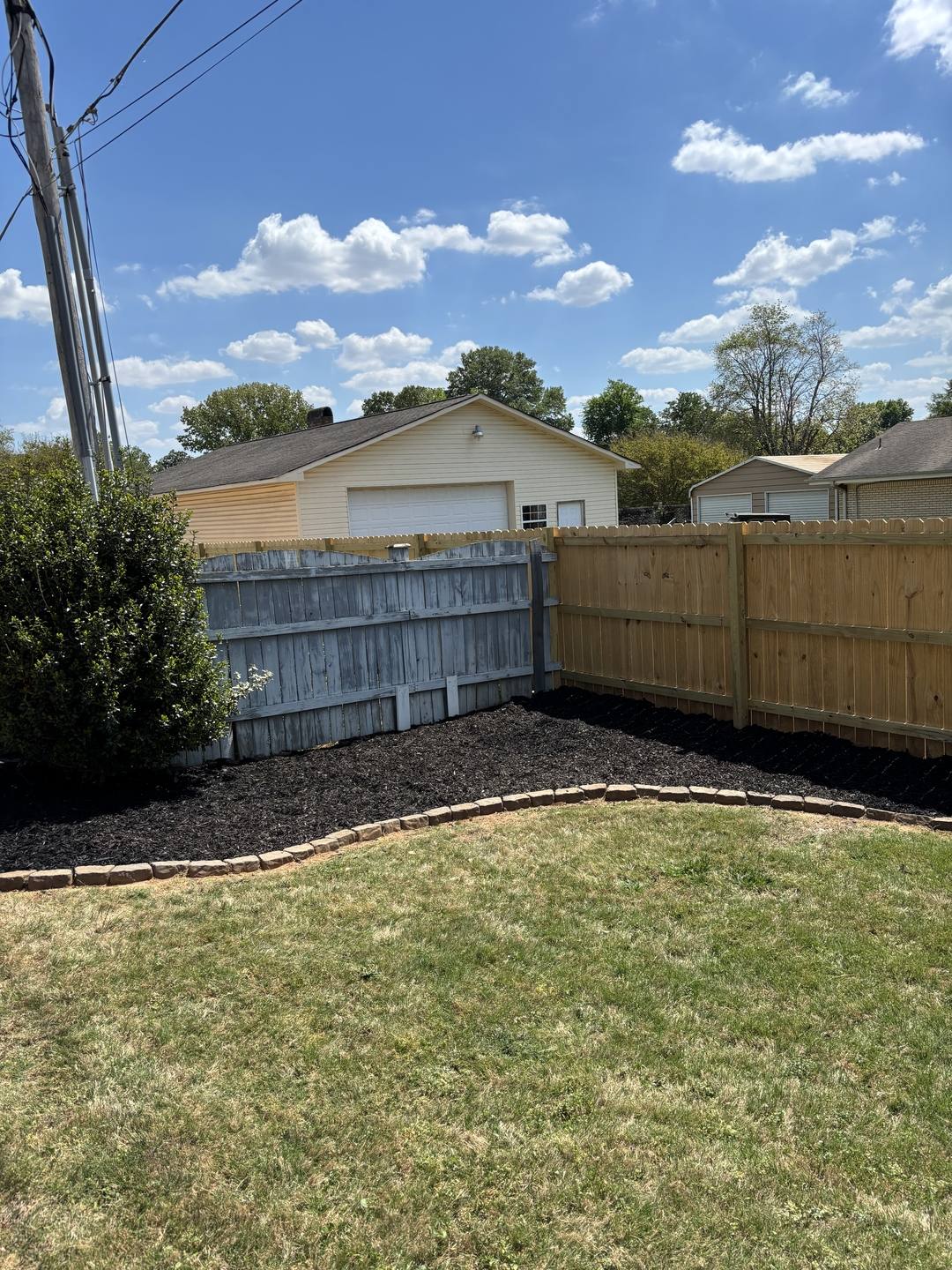 Backyard with a new wood privacy fence and a fresh black mulch bed edged in stone
