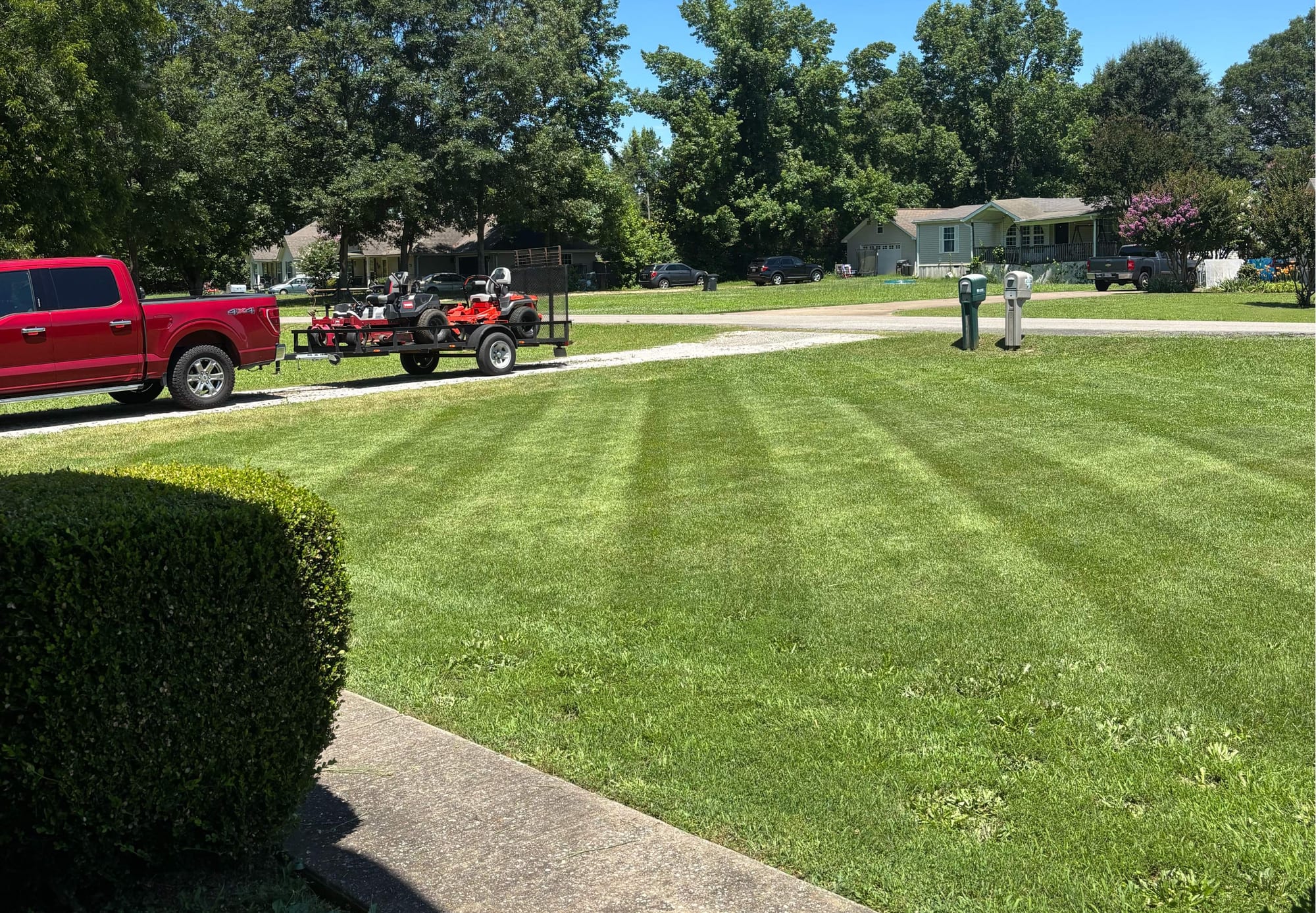 Freshly mowed lawn with crisp mowing stripes and a truck towing a trailer of zero-turn mowers at the curb
